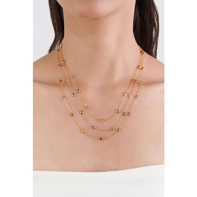 This modern multi-strand station necklace showcases 13.32 carats of natural multicolor sapphires, set in 18K yellow gold....