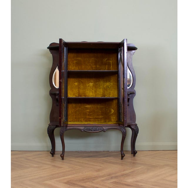 A late Victorian mahogany display cabinet featuring glazed double doors with flowing carved decoration, bevelled teardrop...