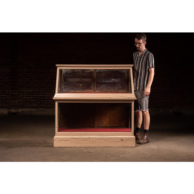Early 20th-century painted wood commercial display case featuring a slant-front glazed upper showcase above a rectangular...