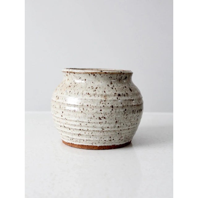 A beautifully handcrafted vintage studio pottery jar featuring a speckled off-white finish, ridged surface design, and a...