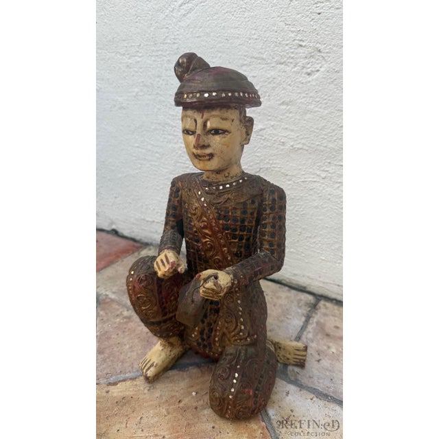 This finely carved Chinese wooden figural sculpture depicts a seated musician holding a small tambourine-style percussion...