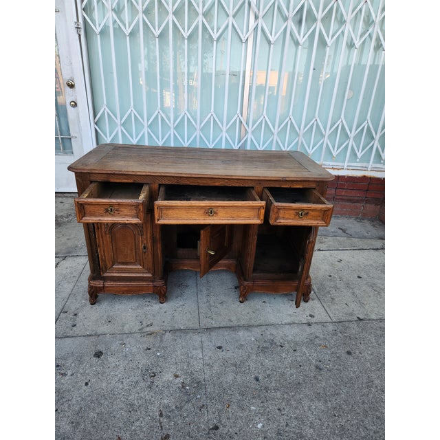 Vintage wooden desk has ornate hand-carved details on the cabinet doors and drawer fronts. This brown oak piece features a...