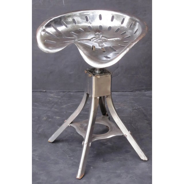 A handsome English tractor seat of polished steel, attached to a revolving four-legged stool stand. The seat has...