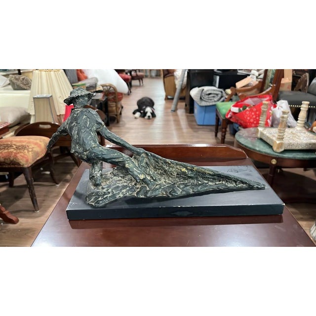An expressive, dynamic sculpture depicting a fisherman leaning forward while hauling in a heavy net. Featuring a weathered...
