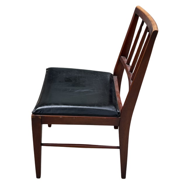 Handsome vintage wood side chair featuring a warm, dark-stained frame and a sleek black upholstered seat. The chair has a...