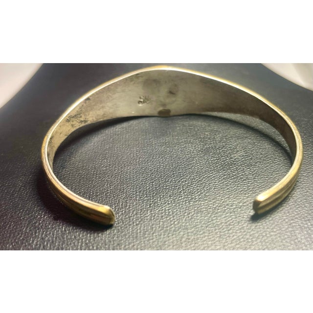 This vintage cuff bracelet crafted by Navajo artist Silver Ray, and signed R. Silver. The bangle features a symbolic...