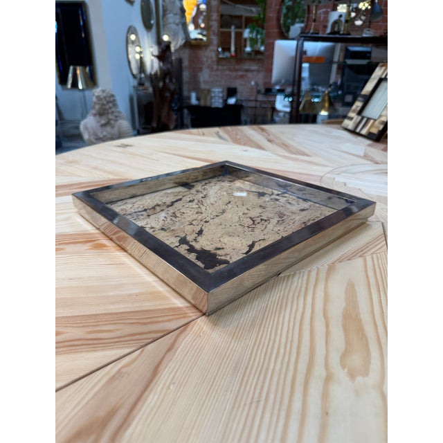 Elegant square tray featuring a cork surface beneath glass, framed by a wide silver-tone metal border. The cork’s organic...