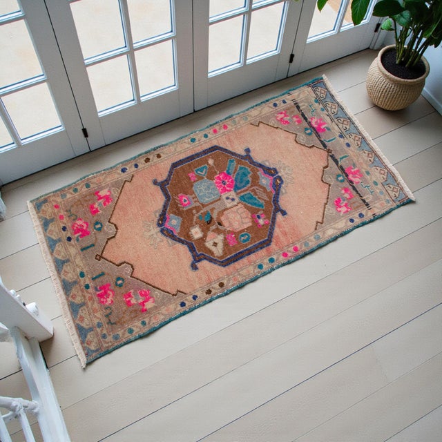 This charming vintage Oushak mat features a sun-faded apricot field anchored by a distinctive central medallion. Its...