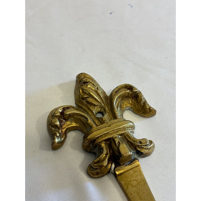 A beautifully cast vintage solid brass wall hook featuring an ornate Fleur-de-Lis backplate and a substantial curved hook....