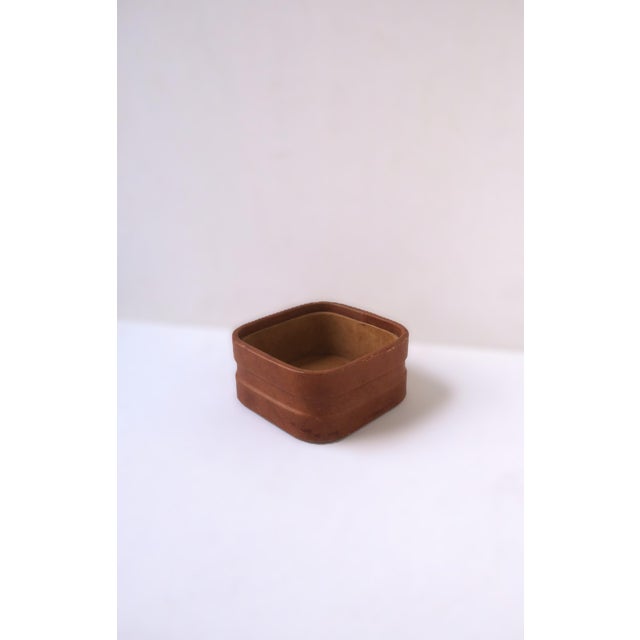A light brown/tan leather and suede jewelry catchall, Postmodern design, circa late-20th century. A square leather and...