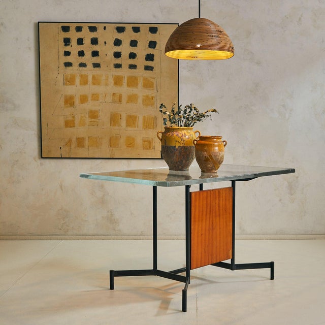 A 1950s Italian desk or console with architectural lines and a grounded presence. The iron base flares outward in a winged...