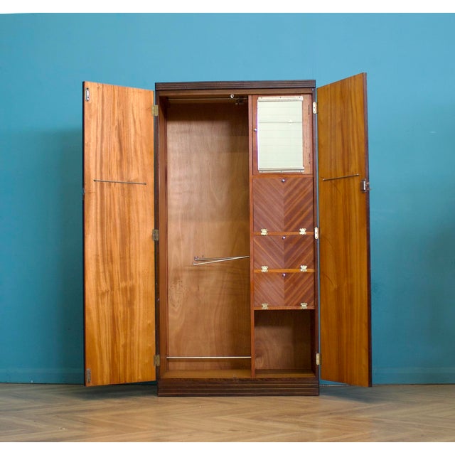 A 1950's compactum double wardrobe in ribbon-grain mahogany veneer. Plain front with central lock and stepped plinth. Left...