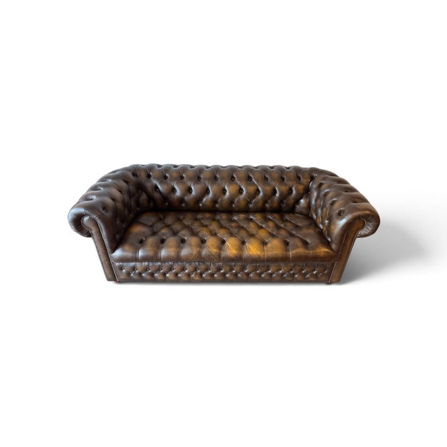 Classic English Chesterfield sofa upholstered in rich brown and dark green leather with deep button tufting, rolled arms,...