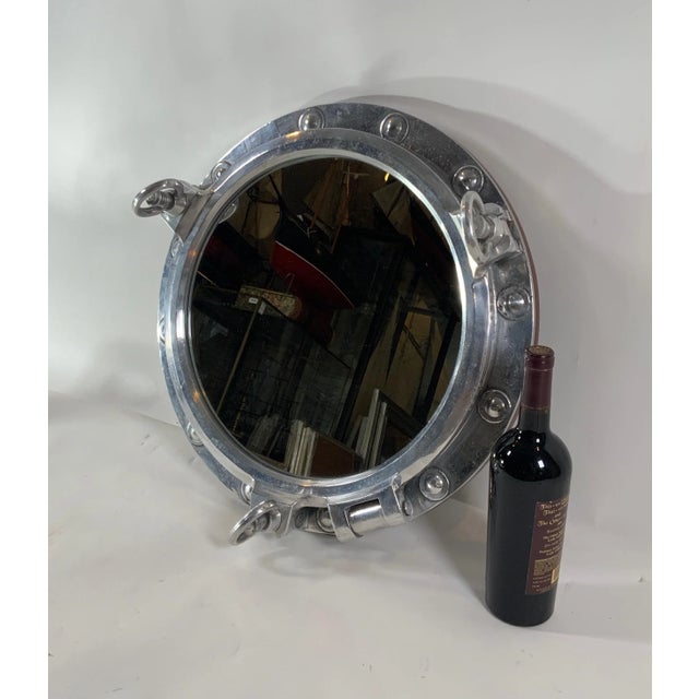 Massive authentic polished aluminum ship's porthole fitted with a glass mirror. Door is hinged and fitted with three...