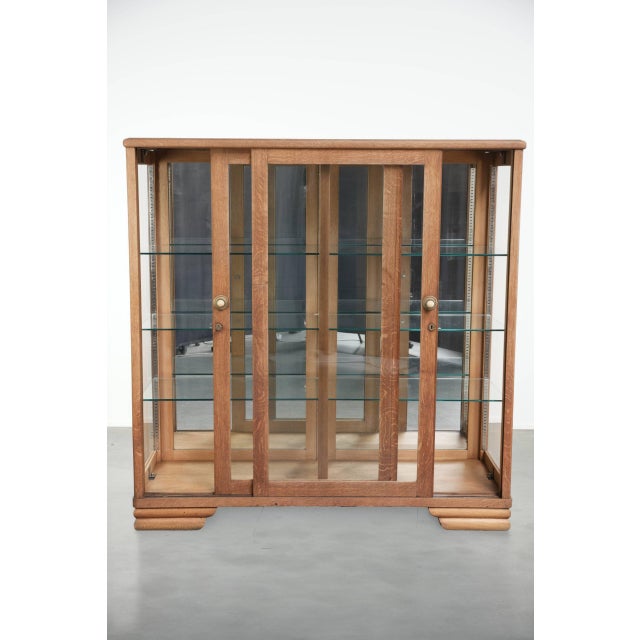 This antique dutch oak display cabinet features two doors, glass shelves, and a mirrored back panel, which creates a sense...
