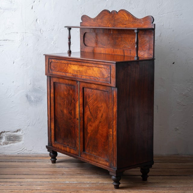 An English mahogany chiffonier with an upper shelf, shaped gallery back, and one drawer with a concealed spring-release...
