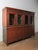 This substantial two-part wooden cabinet features a classic glass-front upper section paired with a paneled lower storage...