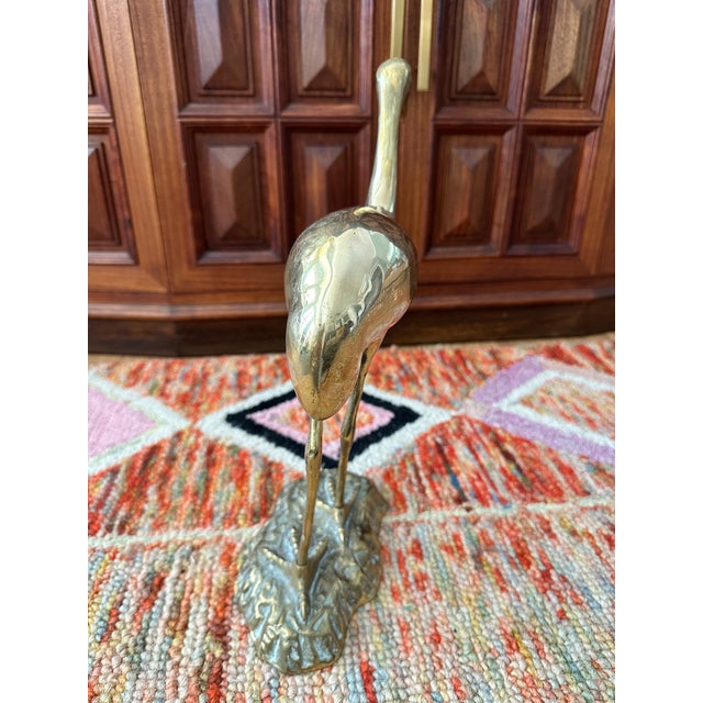 Elegant cast-brass crane standing on a textured base, with a smooth polished body and graceful modernist lines. A timeless...