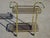 Gold-tone metal serving cart with a flattened tubular frame and smoked glass shelves. Two tempered glass shelves framed by...