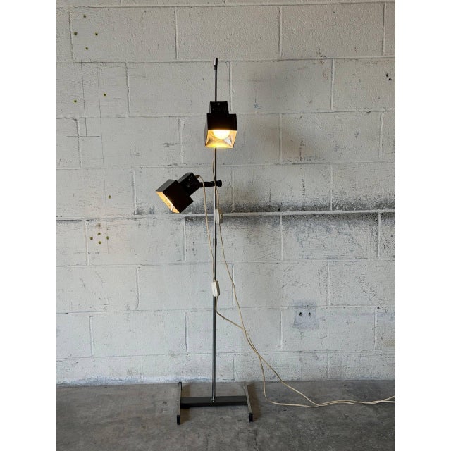 This adjustable metal floor lamp features two directional square shades mounted on a sleek chrome stem. It delivers...