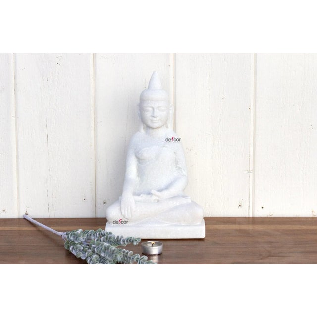 Truly of piece of art, this beautiful hand-carved statue of a sitting Buddha in pure white marble has finely carved facial...