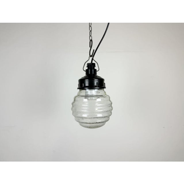 Vintage industrial light made in former Soviet Union during the 1970s. It features a brown bakelite top and a ribbed glass...