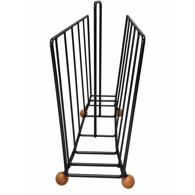 A stylish vintage mid-century magazine rack featuring a minimalist black-painted wire frame, integrated carrying handle...