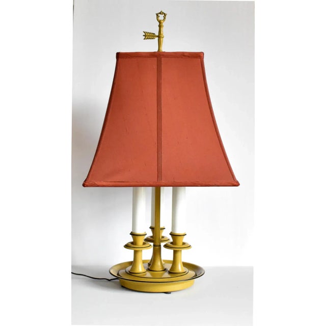 A vintage tole bouillotte electric lamp in an aged mustard yellow base, with white candle sleeves, and a rust red square...