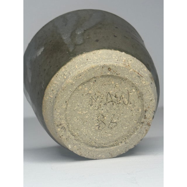 A small handmade studio pottery cup with a rich, variegated dark ash glaze that breaks to lighter tones where it pools and...