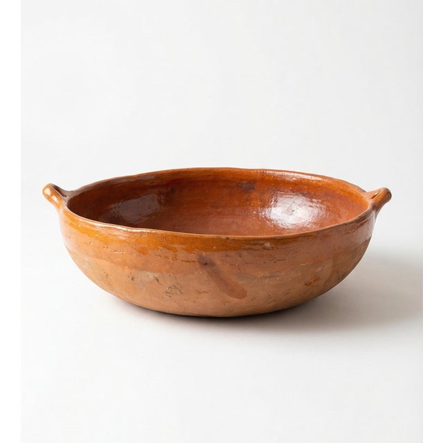 Rustic glazed terracotta serving bowl with integrated side handles. Warm clay tone with subtle tonal variation and light...