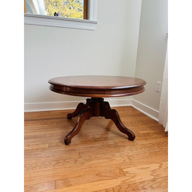 A handsome round wood coffee table featuring a substantial molded edge and a sculptural pedestal base with four sweeping...