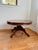 A handsome round wood coffee table featuring a substantial molded edge and a sculptural pedestal base with four sweeping...