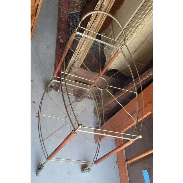 Fine 1950s mid-century modern wood and gold tone metal bar cart. Features two levels of glass shelves, teak wood and brass...