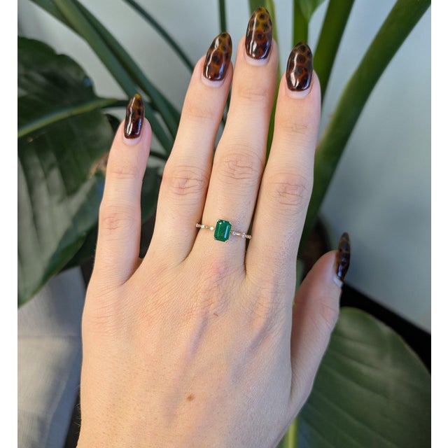 A 1.21ct zambian emerald emerald cut ring set in solid 14K yellow gold, set with six earth mined diamonds. Emerald, the...