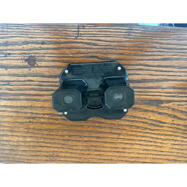 An intriguing vintage black optical viewing device featuring a molded housing, dual viewing lenses, and a small mechanical...