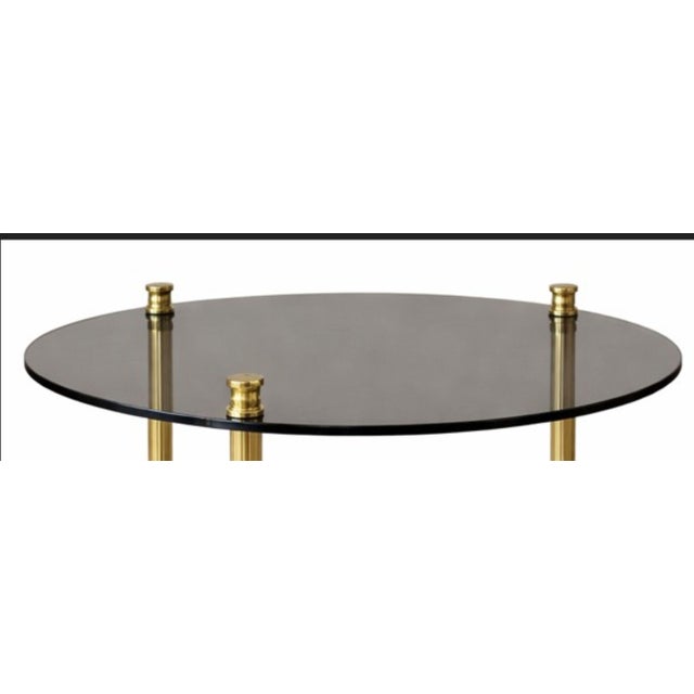 Elegant round coffee table in brass and tinted glass, composed of two glass tops supported by a cylindrical brass frame....