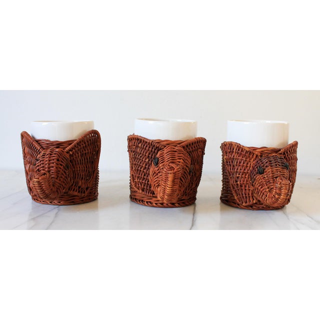 Set of three vintage wicker elephant cup holders with ceramic inserts. Some age wear to wicker. One elephant is missing...