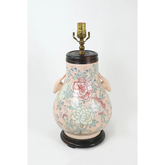 A famille rose vase lamp with animal head handles and blooms of flowers in various colors against a soft pink background.