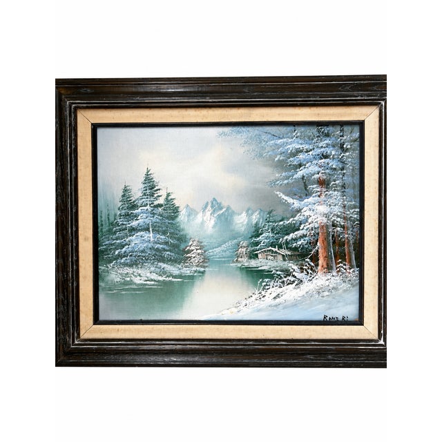 A signed landscape painting depicting a tranquil mountain lake surrounded by snow-covered evergreens, distant alpine...