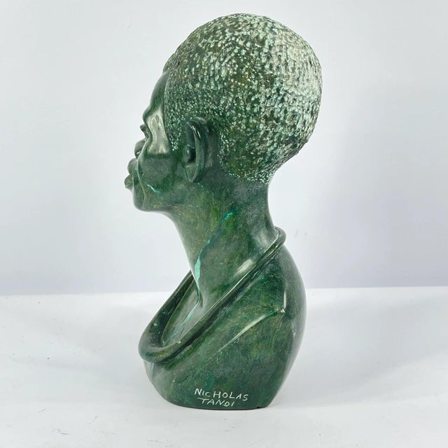 This hand-carved stone bust by Nicholas Tandi depicts a male figure with expressive facial features and textured hair,...