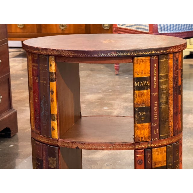 Cylindrical two tier book table, the drum faced with tooled leather book spines in shades of red, tan, and brown with gilt...