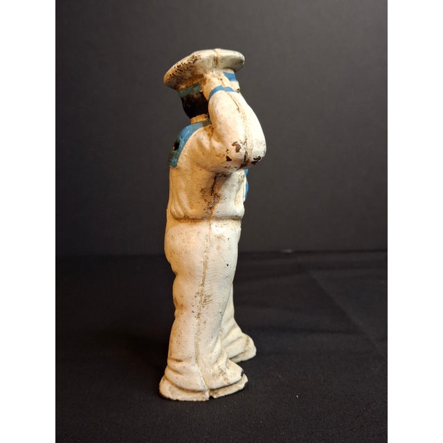 This authentic antique American cast iron still penny bank depicts a saluting U.S. Navy sailor (or oarsman) holding an oar...