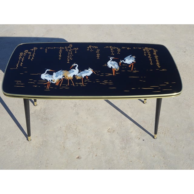 A unique black and gold coffee table featuring a design of grey herons on the tabletop. The rectangular tabletop has...