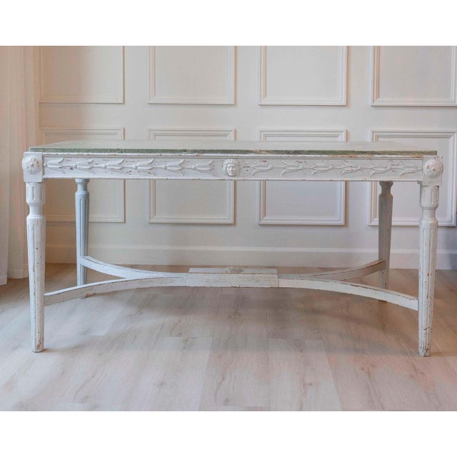 Swedish 1920s painted center table with a restrained neoclassical silhouette and original green marble top. The hand-...