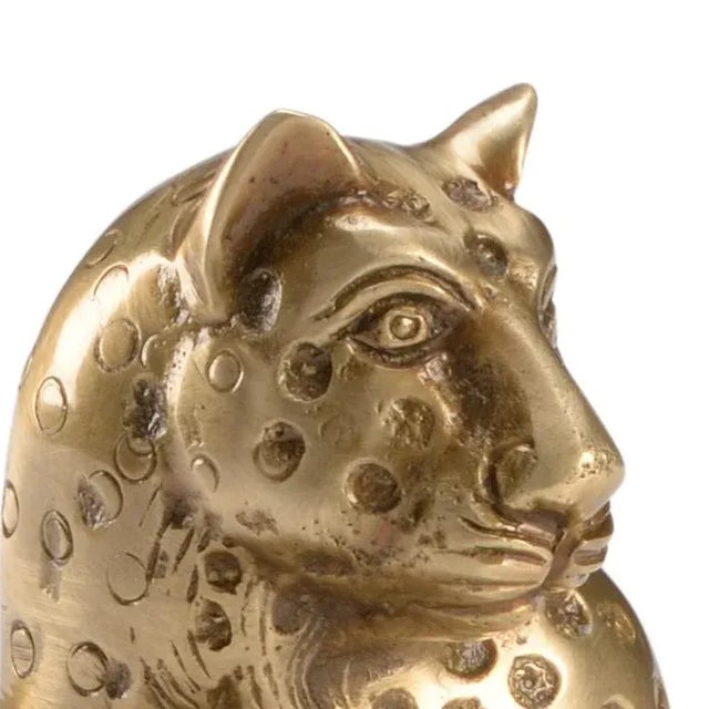 Brass leopard sculpture sitting on a black leaf beside a brass leaf votive.
