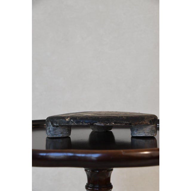 A hand-carved footed chapati board, used in Indian kitchens for rolling dough, with a worn surface and rich patina. Use it...