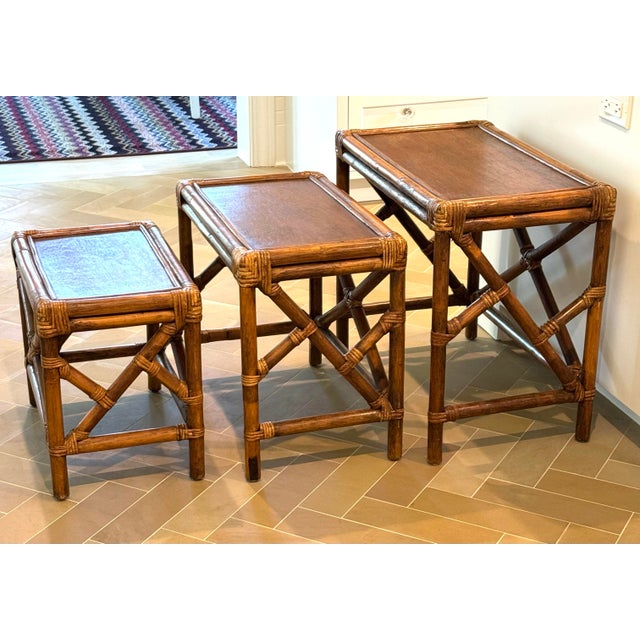 A beautifully crafted set of three vintage nesting tables featuring warm honey-toned rattan construction with rich inset...