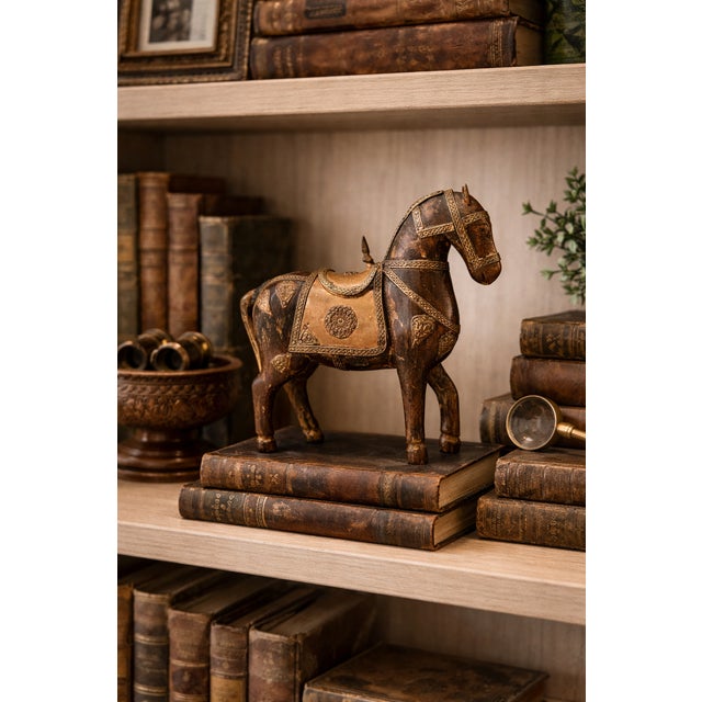 A vintage carved wood horse sculpture decorated with etched metal inlay and detailed saddle ornamentation. The warm aged...
