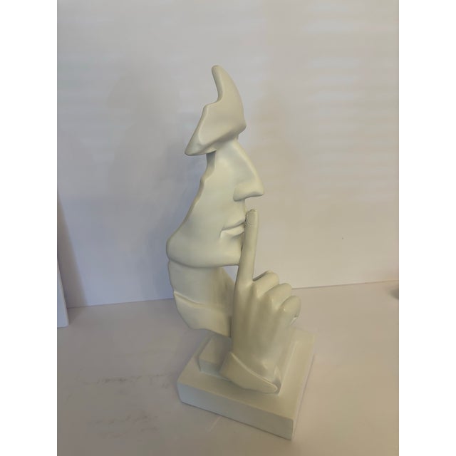 Stark white. A minimalist sculpture made in the early 21st century out of resin gives a Shhhhh… with a finger pressed to...