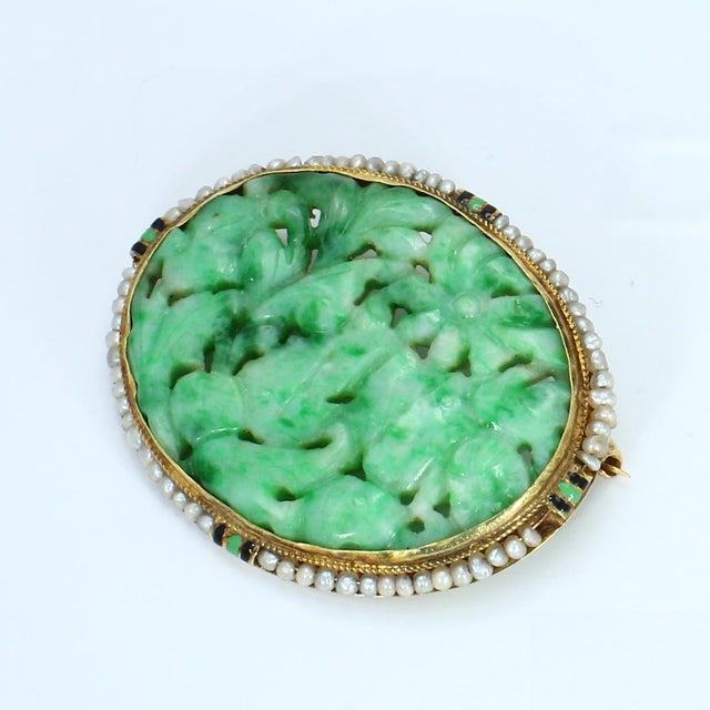 This oval brooch features an intricately carved green jade centerpiece, surrounded by a border of small pearls. The...